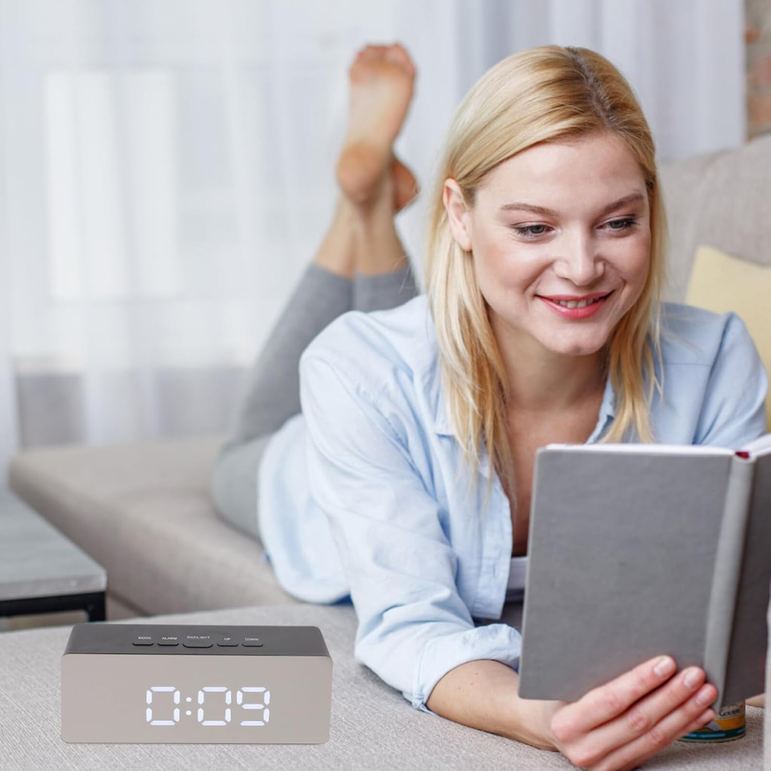 A Woman is Reading Book and a LED Digital Alarm Clock with Mirror Display is Placed Next to Her.