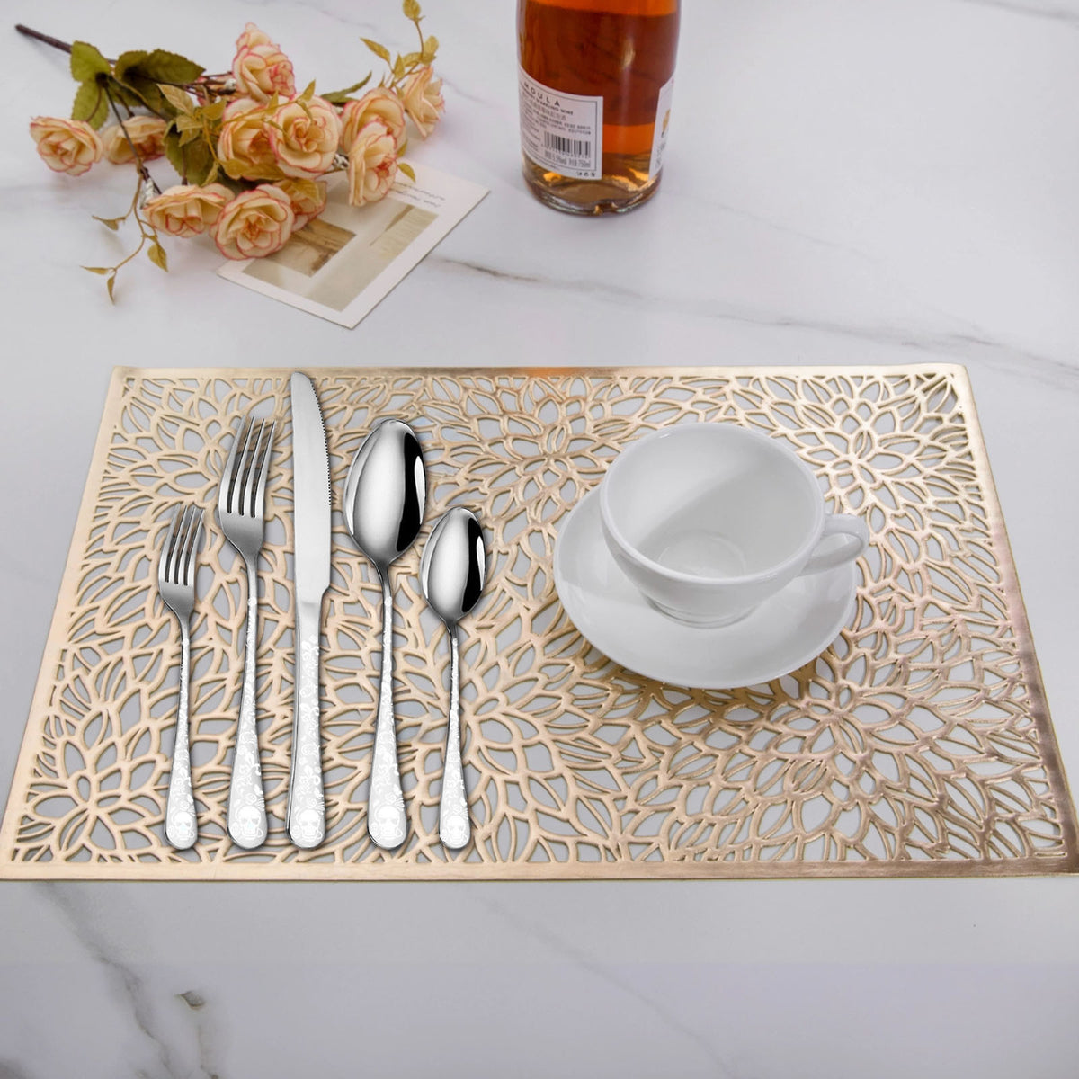 Decorative placemat with cut-out patterns, silverware, and a cup on a table.