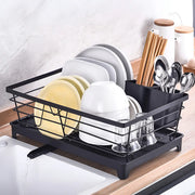 Black dish drying rack with plates, glasses, and utensils on a kitchen counter.
