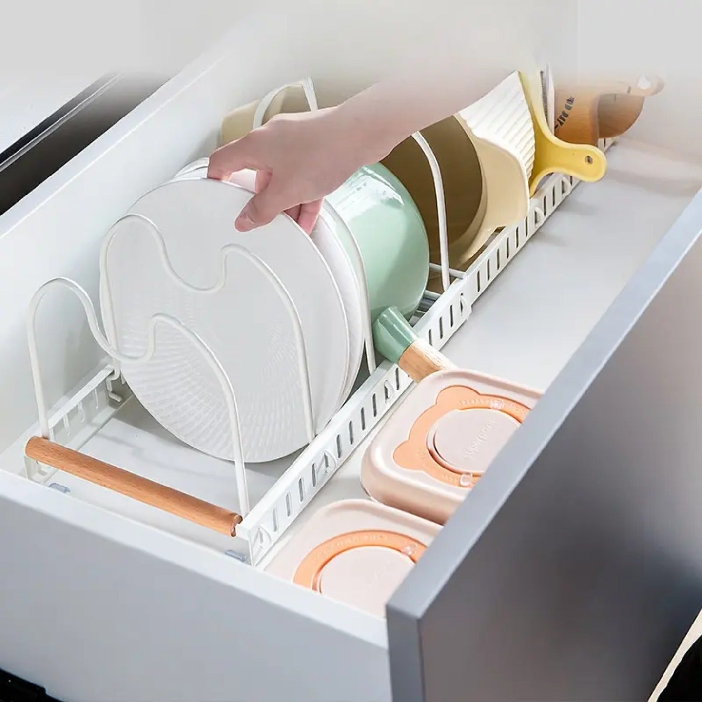 A Person is Taking Utensils From Expandable Pot and Pan Organizer Rack Organized with Pans and Plates.