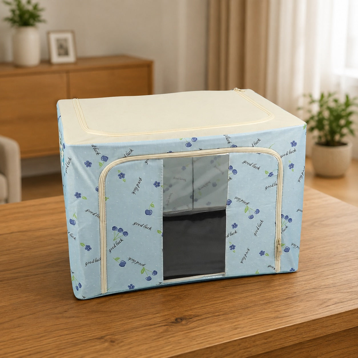 A Foldable Cloth Storage Organizer Box with a cherry and script pattern, featuring a clear zippered window, placed on a wooden table in a living room setting.