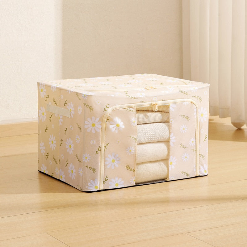 A Foldable Cloth Storage Organizer Box with a white daisy floral print and a zippered front window, shown holding folded white towels on a light wood floor.