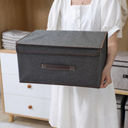 Person holding a Foldable Fabric Storage Box with a brown handle in a room with furniture.