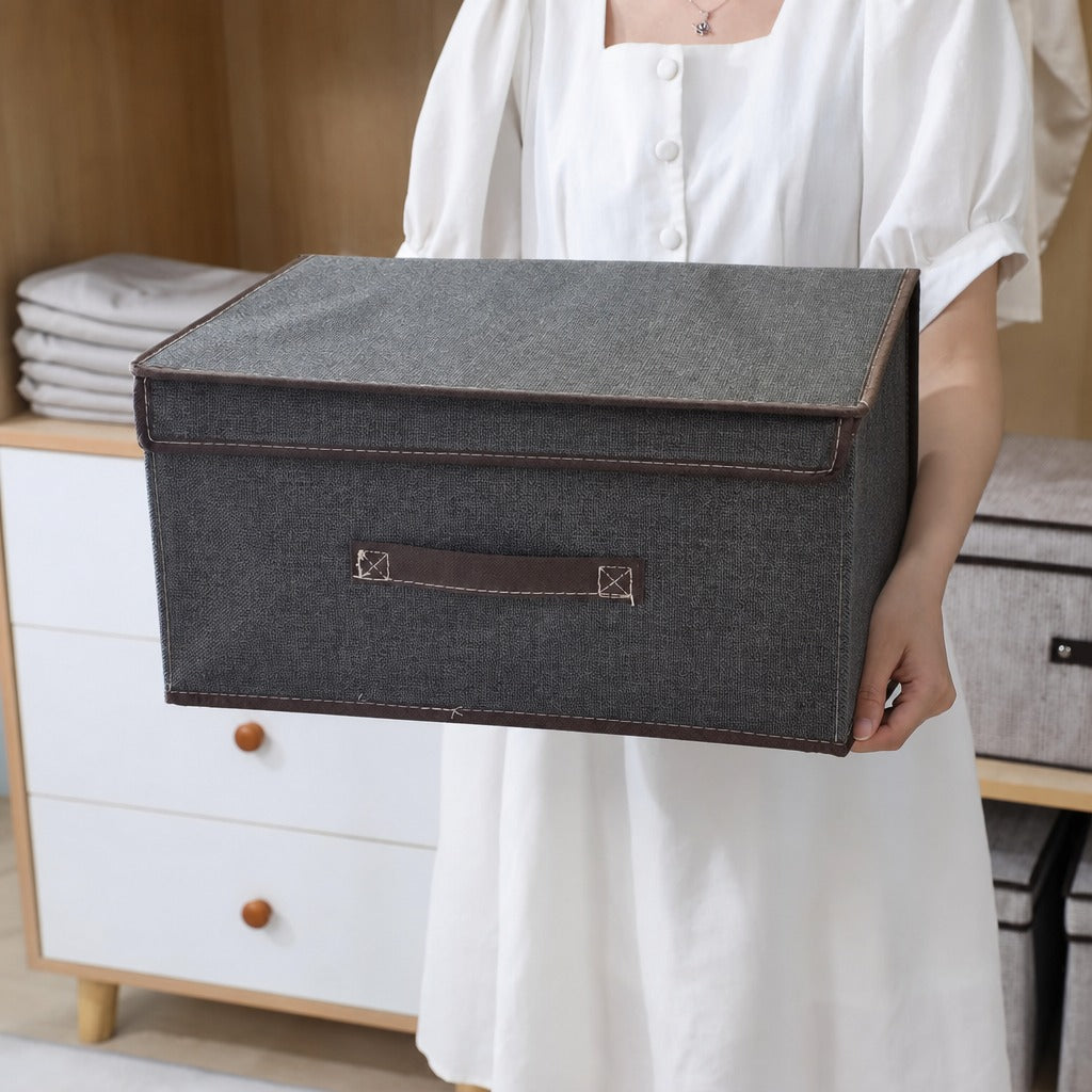 Person holding a Foldable Fabric Storage Box with a brown handle in a room with furniture.