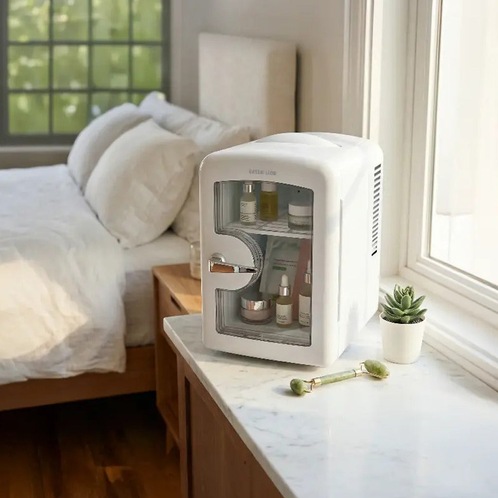 Green Lion 4L Mini Fridge on a nightstand with skincare products inside, next to a bed in a bedroom.