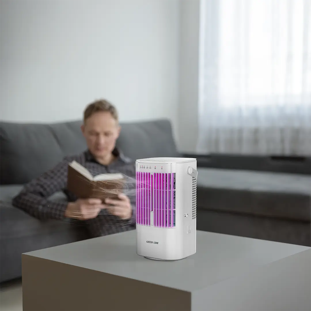 Person reading a book with a Green Lion Compact Air Cooler on a table in the foreground