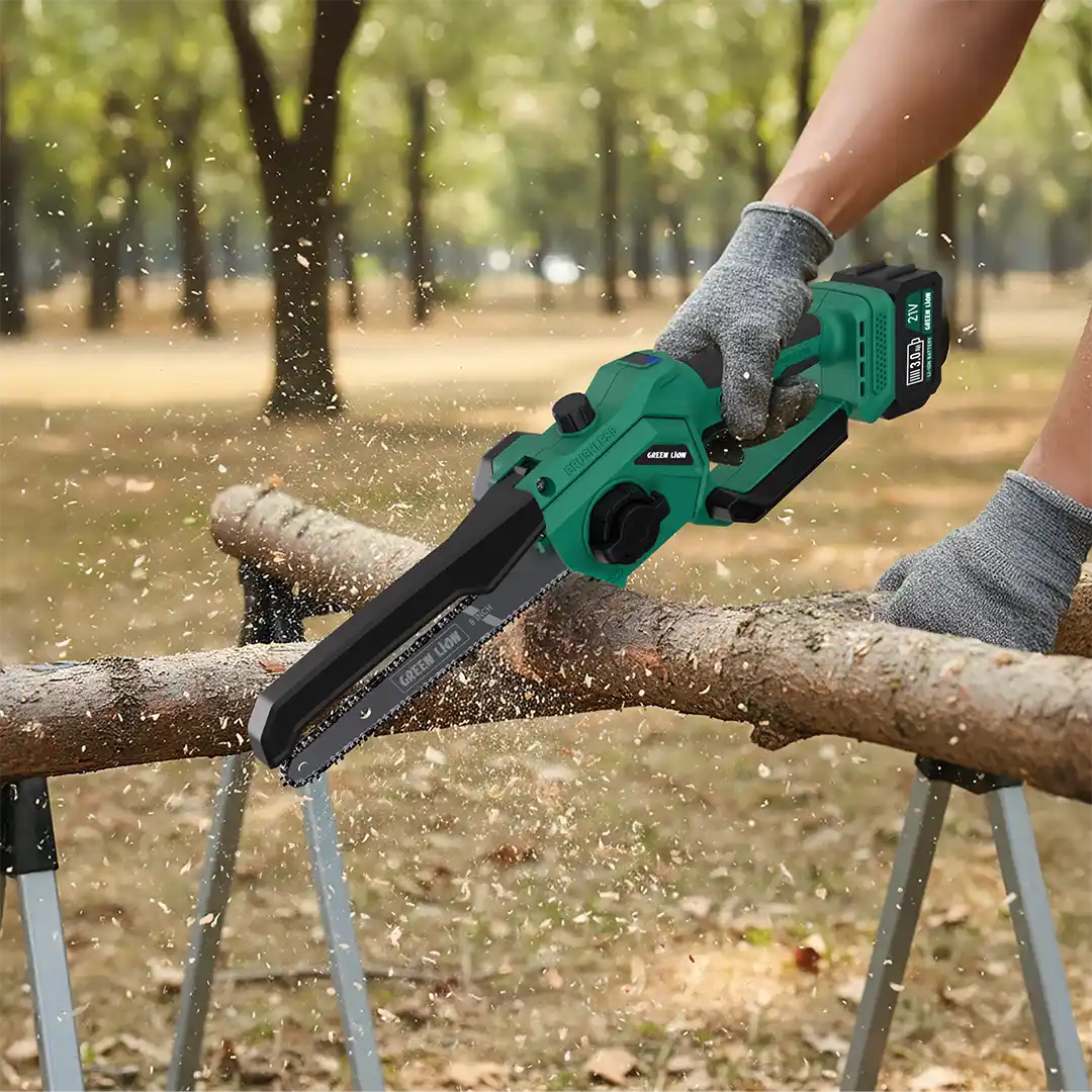 A person outdoors using a Green Lion cordless electric chainsaw to cut a tree branch.