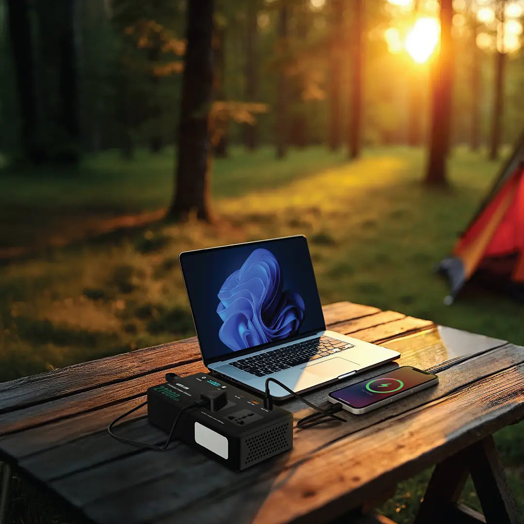 Laptop and smartphone while charging it with the Green Lion Volt Mate 27000mAh Portable Power Station on a wooden table in a forest with sunset