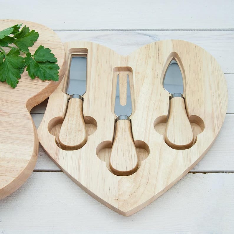 Heart-shaped wooden cheese board with built-in knife storage and serving area for cheese and crackers.