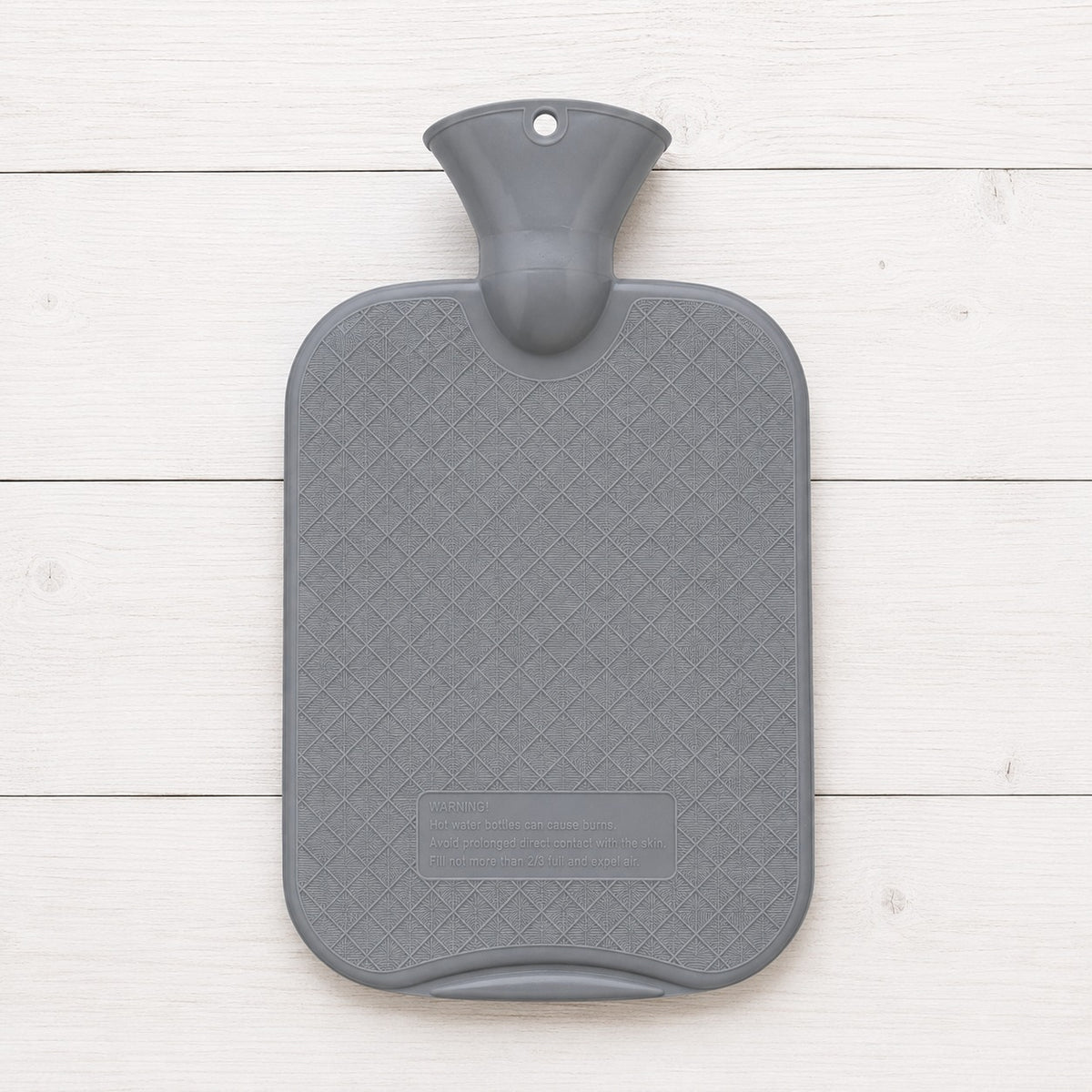 A gray hot water bottle with a textured diamond-patterned surface and a molded handle, shown from a top-down view on a white wood plank background.