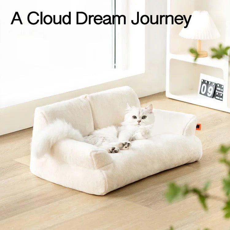 A cat lying on a white color Cat Sofa Couch Cushion next to a shelf with calendar and lamp in a room