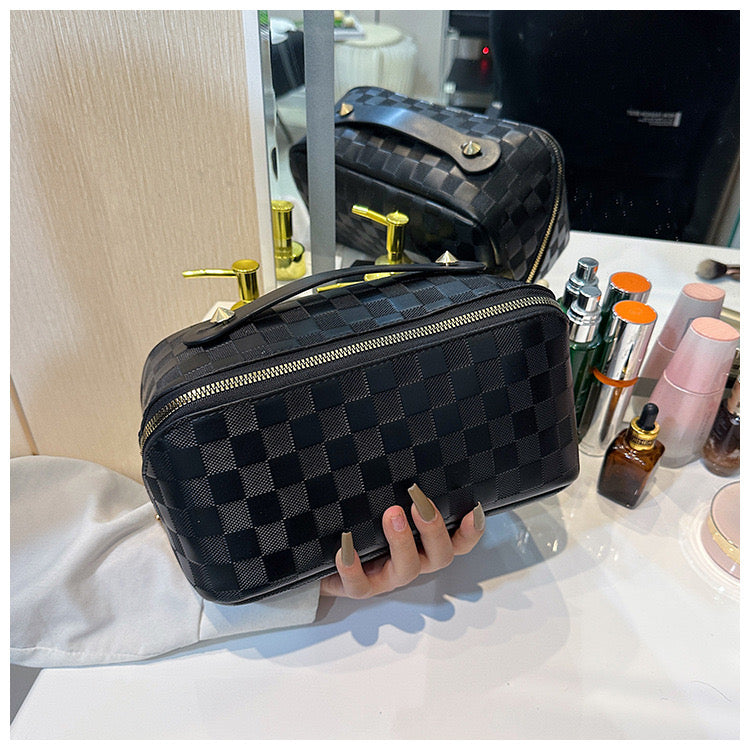 A person tending to lift a Black color Cosmetic Bag from a makeup table with few cosmetic products placed 