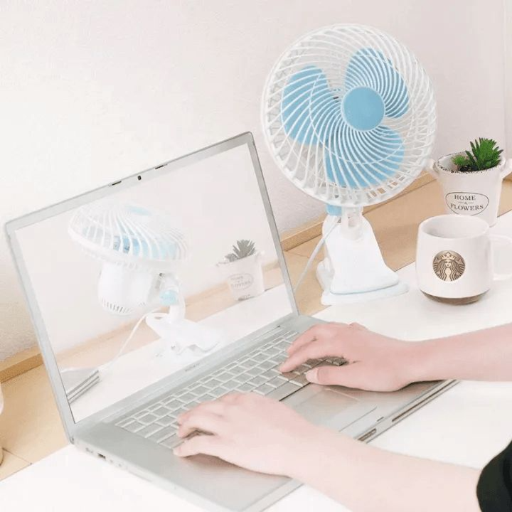 A Person is Using Laptop and a JIHAM 8-Inch Table & Clip Fan is Kept Nearby.