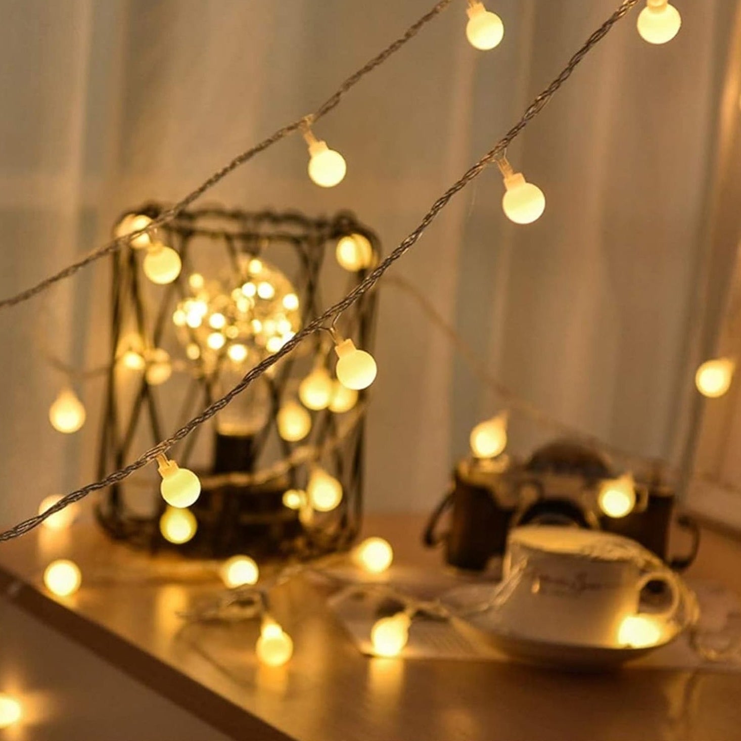 String lights with a teacup and saucer on a table, creating a warm and cozy atmosphere.