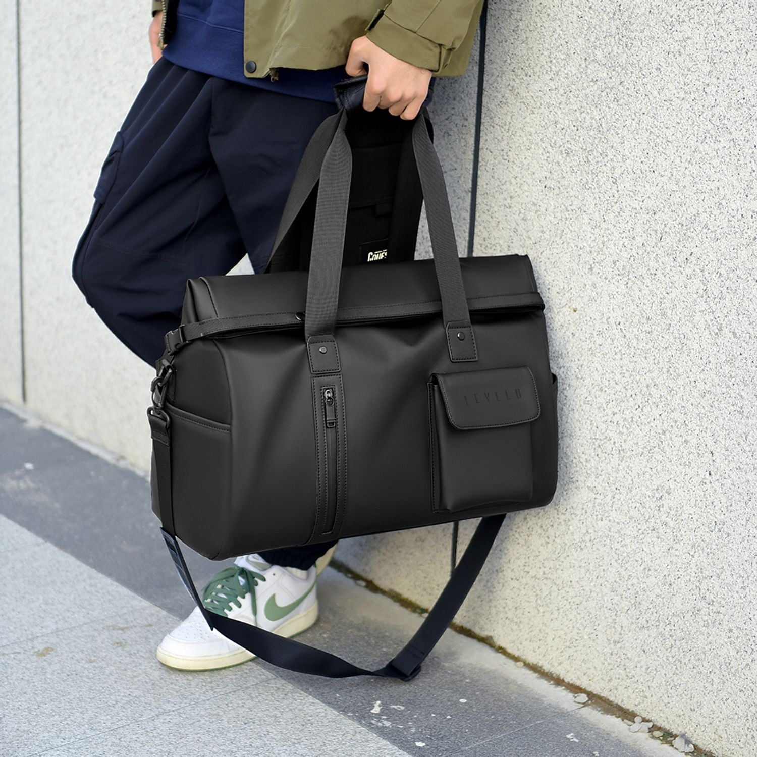 Person holding a LEVELO Monaco Waterproof Travel Duffel Bag against a light gray wall.