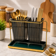 A Luxury Double Cutlery Holder utensil holder with dark translucent gray ribbed cups and a teal tray, shown on a marble countertop in a kitchen setting with gold and silver cutlery inside.