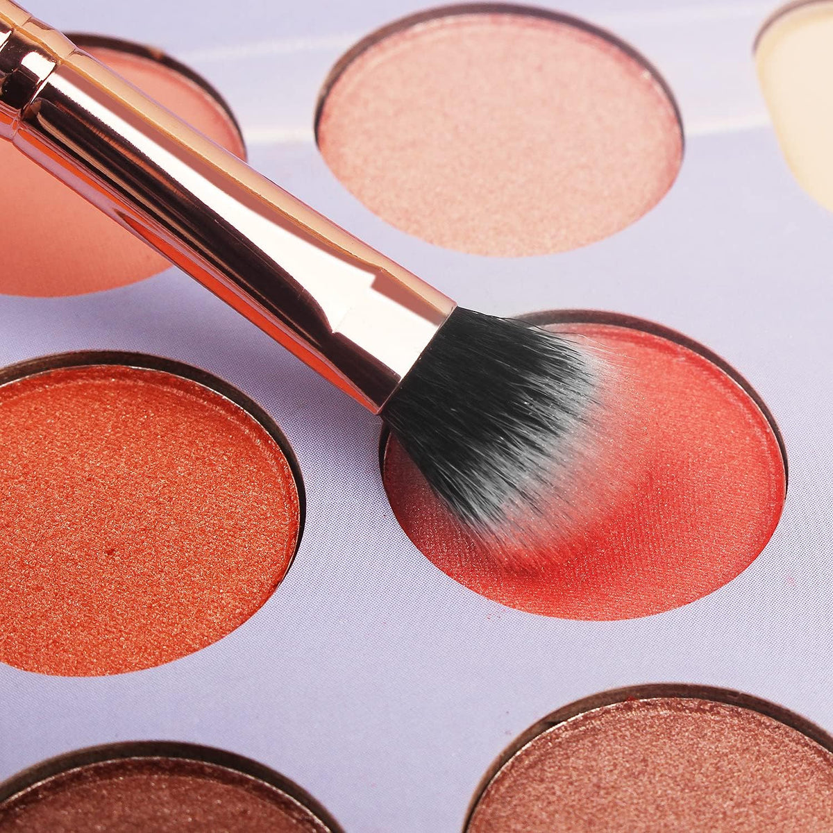 A makeup brush is being used on a palette of eyeshadows from the 16-Piece Makeup Brushes Set Kit with Premium Synthetic Bristles and an Eyebrow Razor