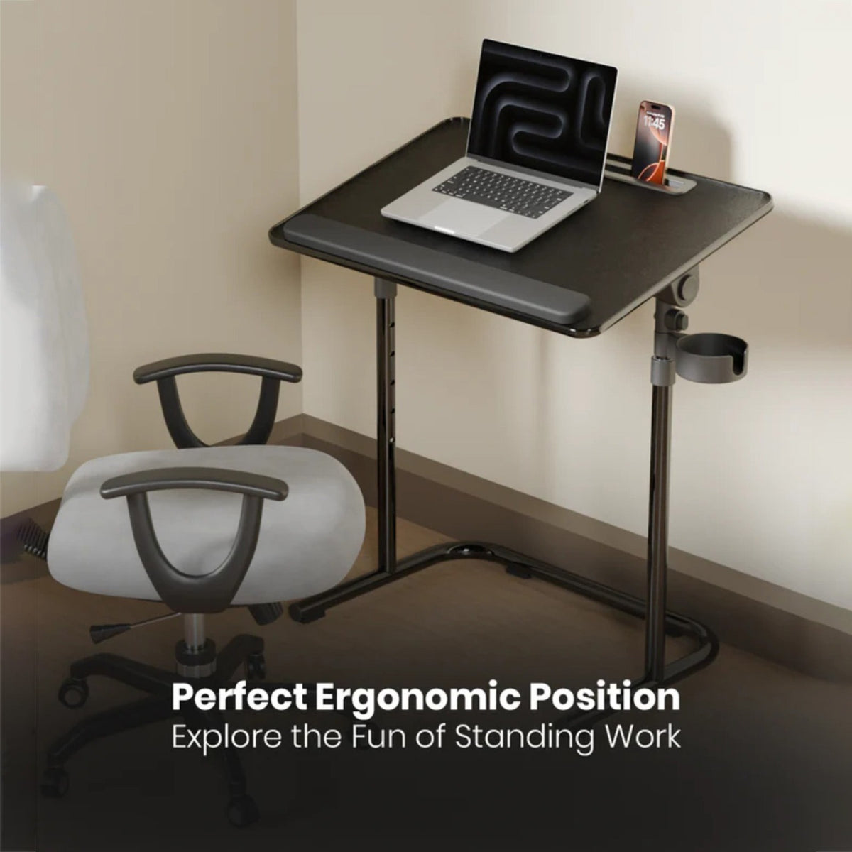 A Moxedo FlexMate Adjustable Height Laptop Desk  with an adjustable black frame and dark gray top, shown in a room corner with a white office chair, a laptop, and a phone on the desk. Text at the bottom reads 'Perfect Ergonomic Position Explore the Fun of Standing Work.