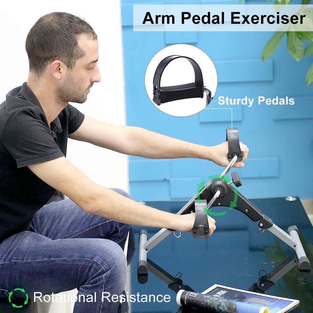 A man is using a compact pedal exerciser placed on a table for an arm workout.