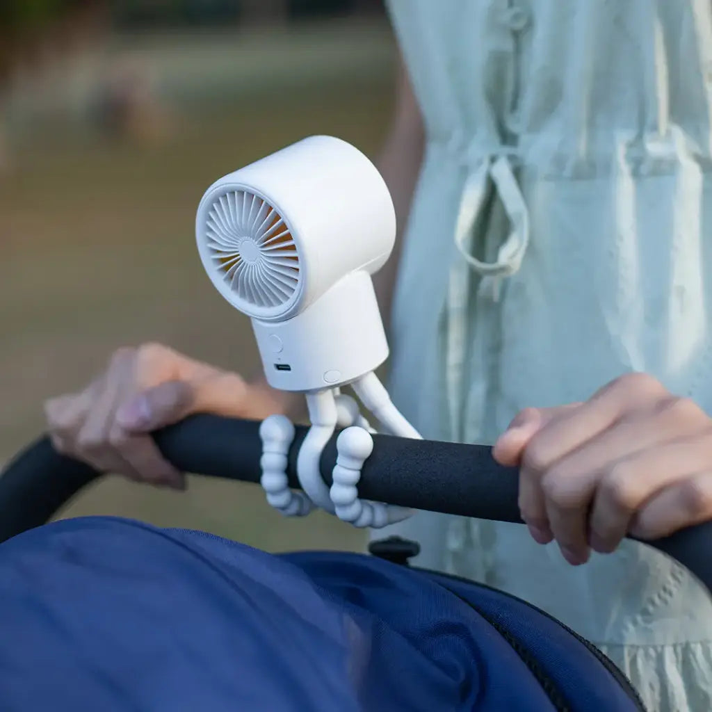 Porodo CoolFlex Mini Handheld Fan attached to a stroller handle with a blurred background