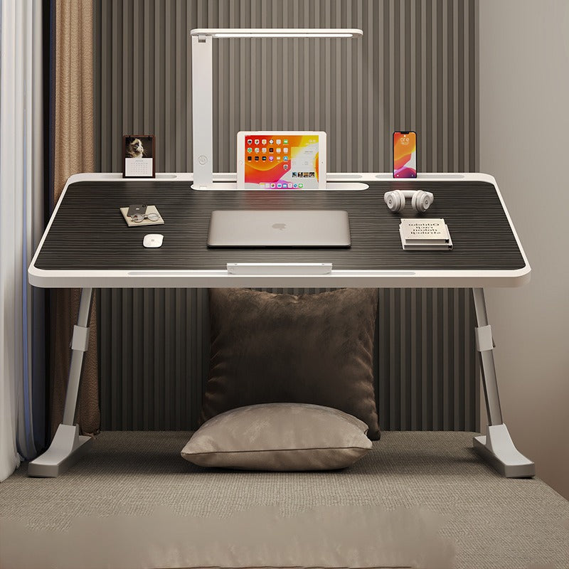 Portable foldable laptop bed desk table with adjustable legs and built-in LED lamp, arranged with laptop and other essentials.