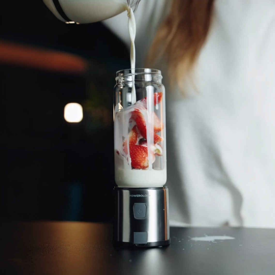 Person pouring liquid into a Powerology 6-Blade Portable Juicer with fruits on a dark surface