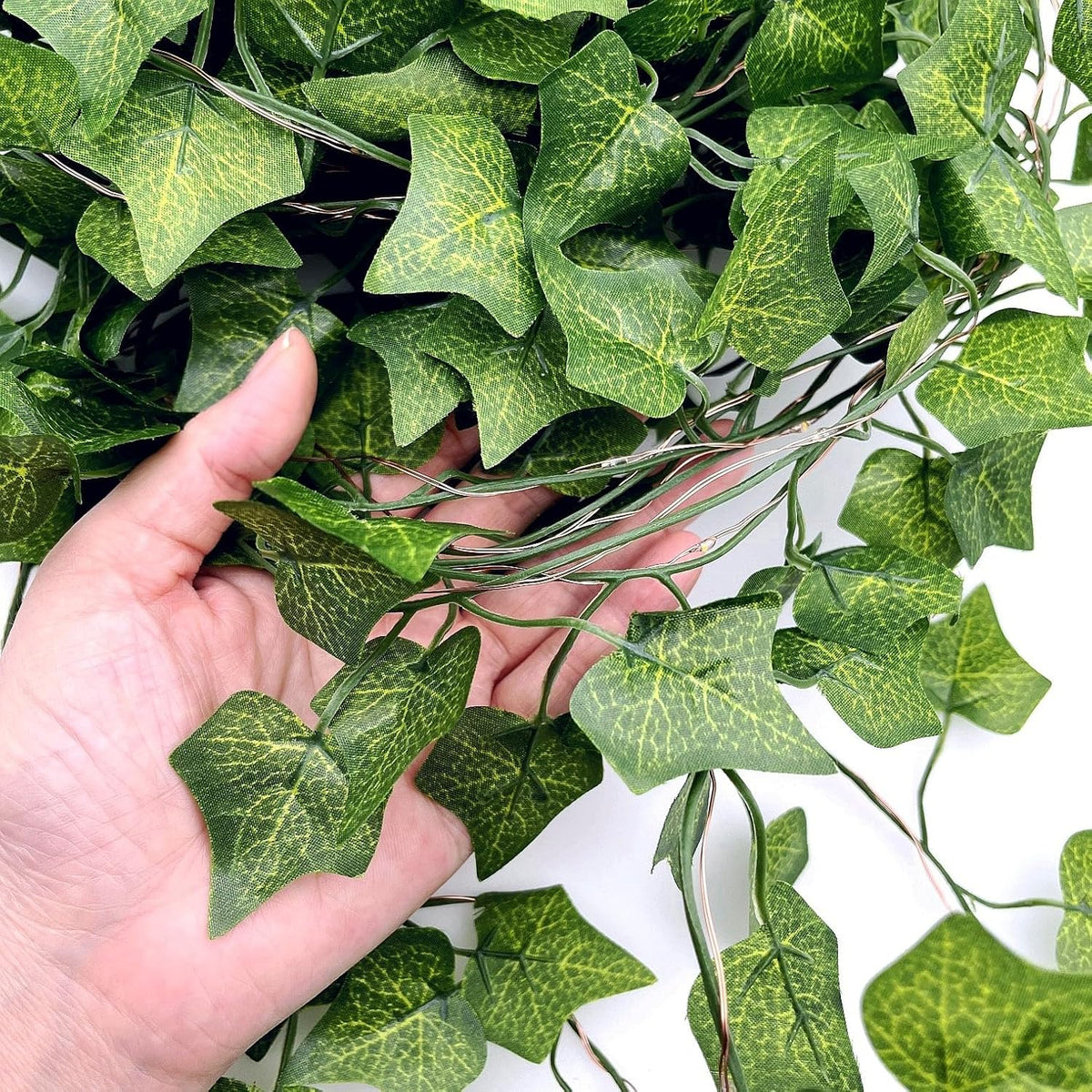 Hand holding a bunch of Artificial Ivy Leaf Garland LED String Lights against a white background