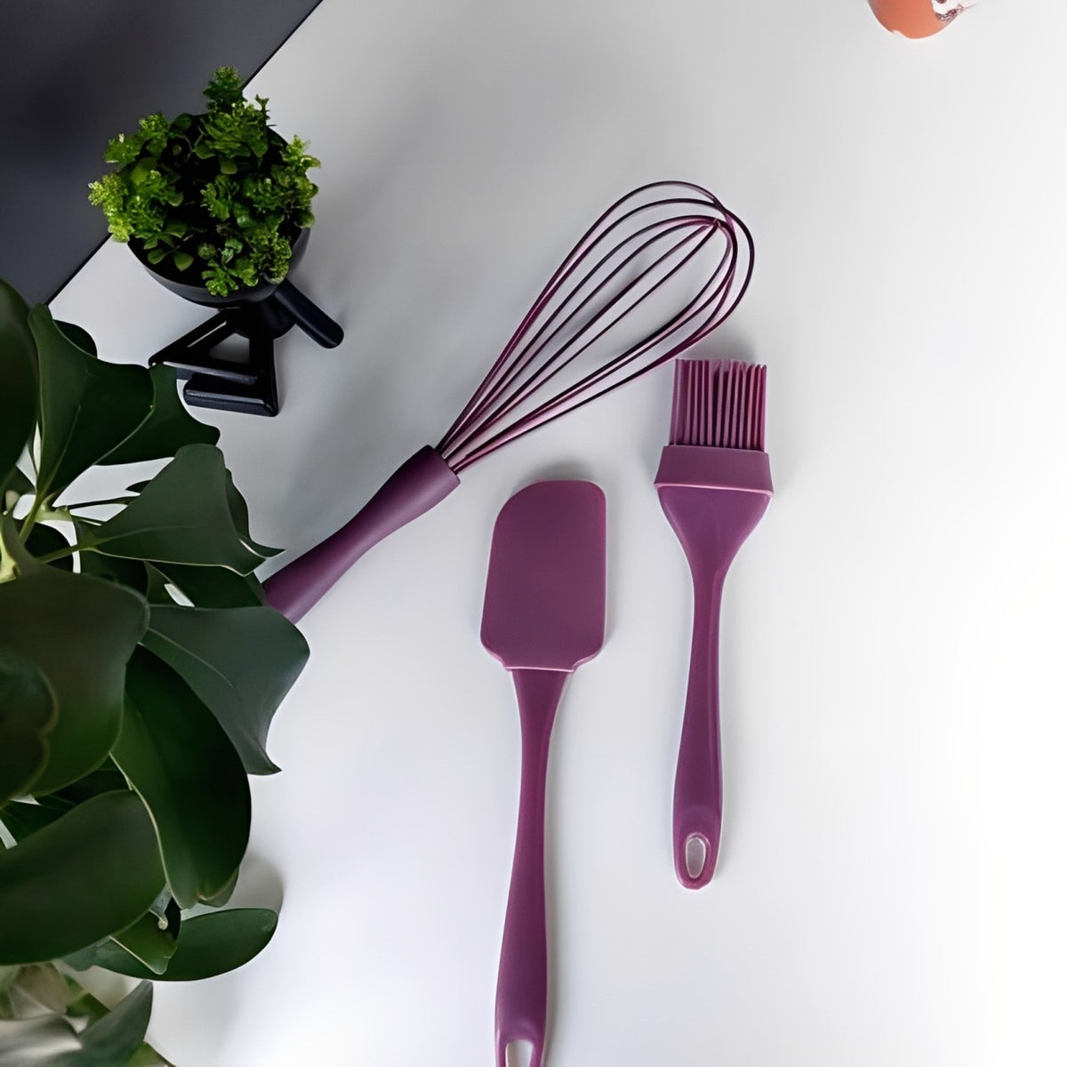 A brush and spatula placed on a white floor, surrounded by green leaves.