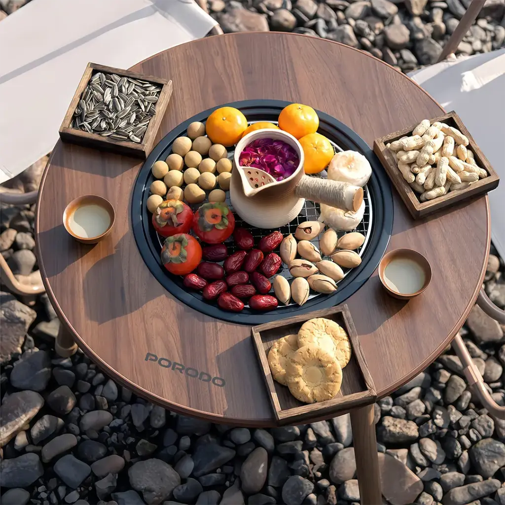Porodo Lifestyle Outdoor Round Grill Table  with various snacks and a pitcher on a rocky surface