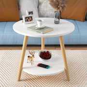 Round white coffee table with wooden legs, holding a cup, book, photo frame, and decor; cherries and a game controller below in a living room