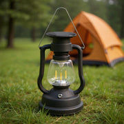 Black vintage-style LED lantern placed on grass with an orange camping tent in the background.