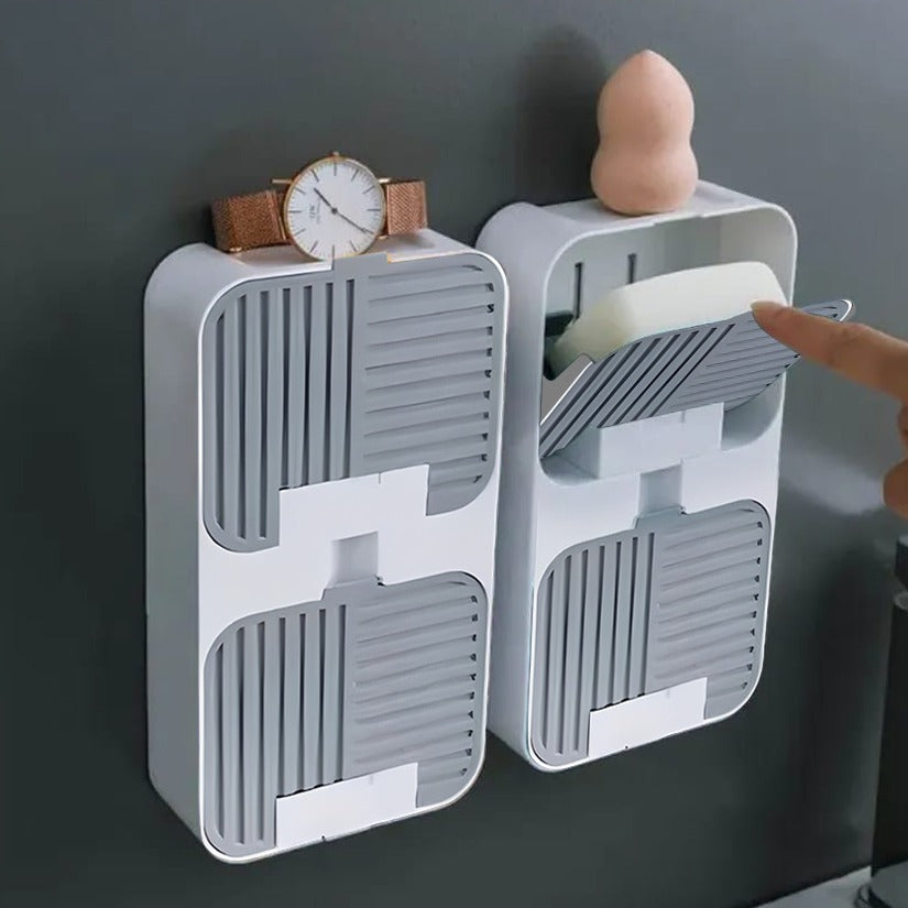 Two Flip Lid Drain Soap Box placed in wall , A person is reaching toward Wall mounted storage container and lifting the flip-top lid to access a bar of soap stored inside .