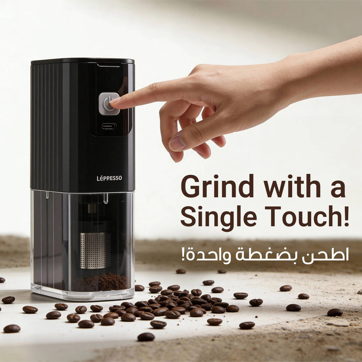 A person pressing the button of a Lepresso JetGrind Rechargeable Coffee Grinder, One-touch operation, compact cordless grinder, premium stainless steel finish, fresh coffee beans inside, cozy kitchen background