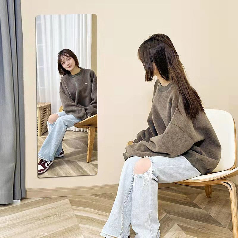 A girl sitting in a chair and looking into HD Self-Adhesive Acrylic Mirror Tiles, captivated by the clear reflection