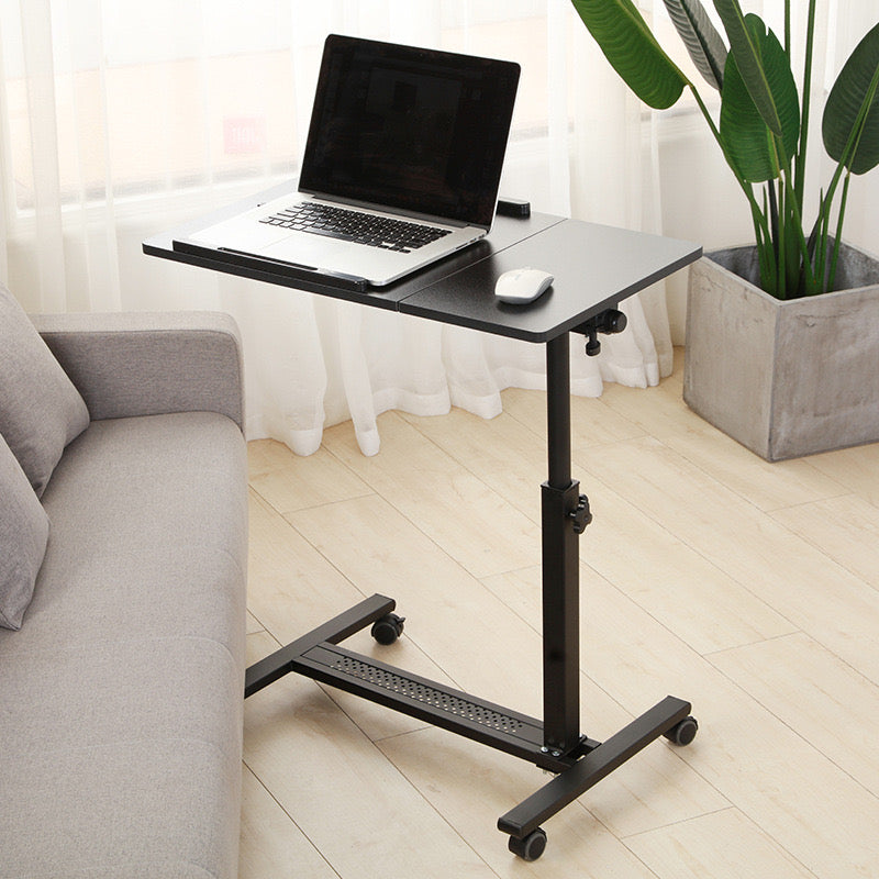 Black Adjustable Overbed Laptop Stand Table with a laptop on top, positioned on the floor beside a sofa