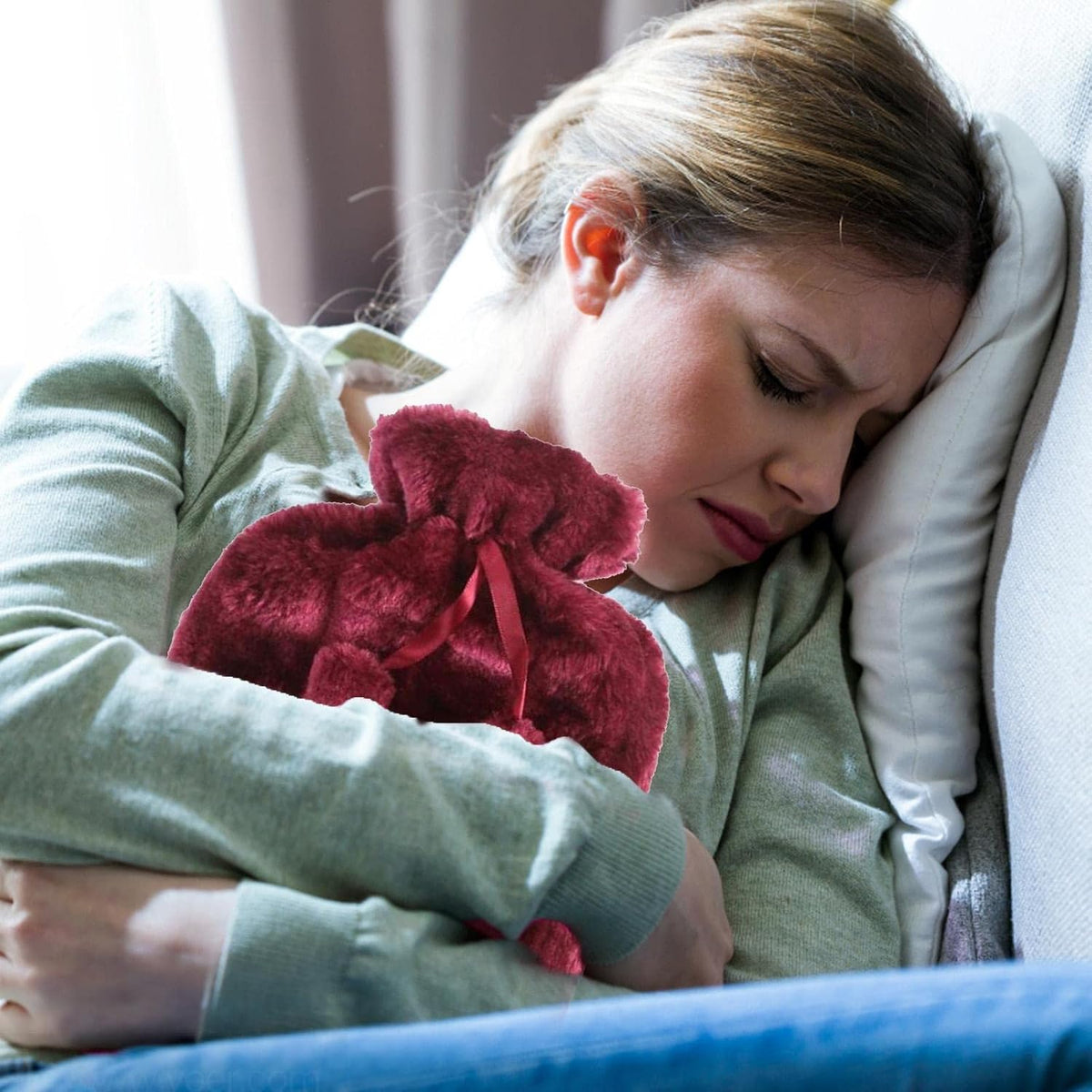 Woman lying in bed holding a Soft Plush Hot Water Bag, wearing a green sweater.