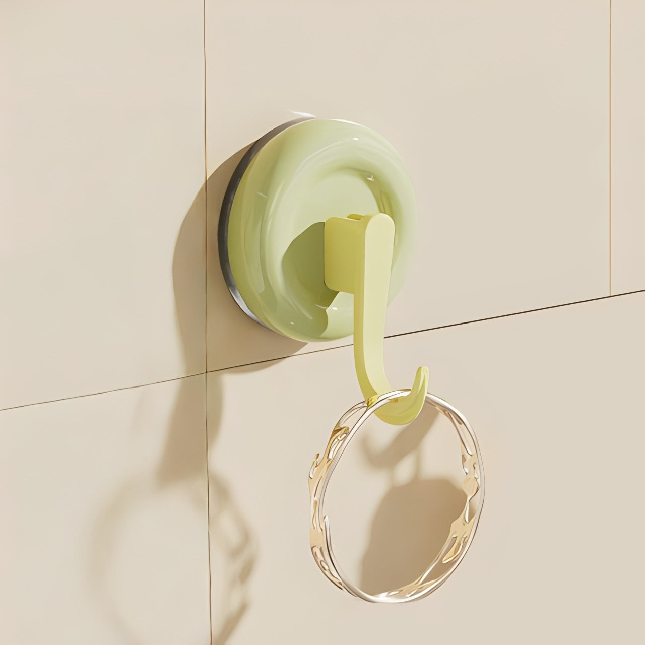 Green suction cup hook on a tiled wall with a gold ring attached.