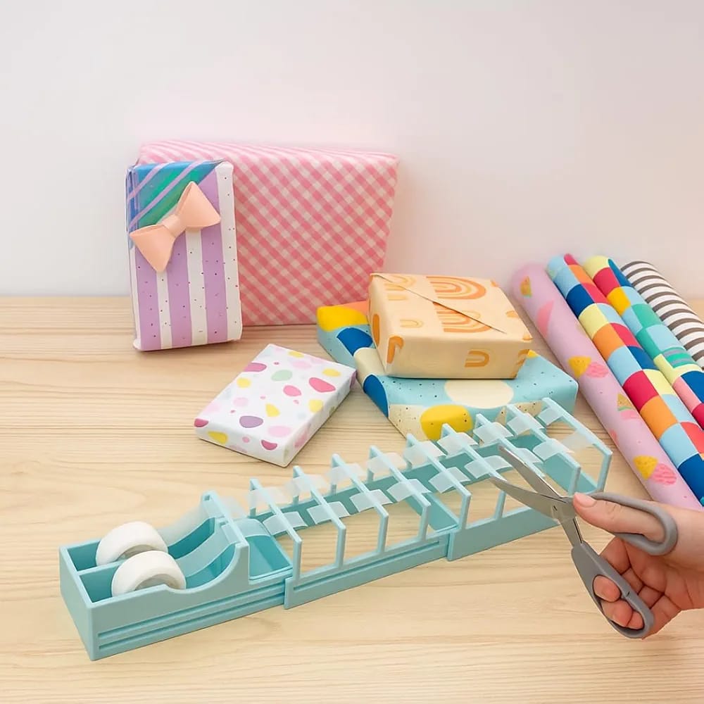 Gift wrapping station with tape dispenser, wrapped boxes, rolls of wrapping paperand a hand using scissors.