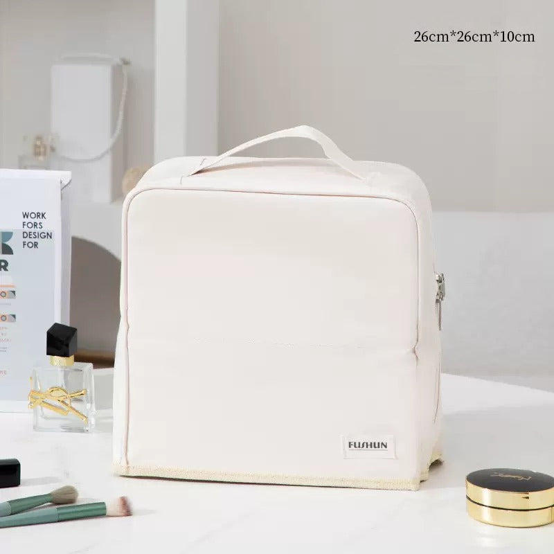 Travel Makeup Bag Cosmetic Organizer Case with a top handle and a small 'FURUN' label on the front, displayed on a white table with cosmetic items and a perfume bottle in the background.
