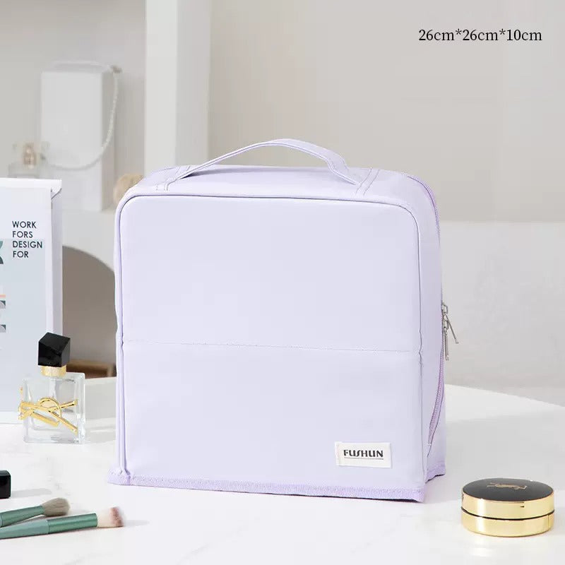 Travel Makeup Bag Cosmetic Organizer Case with a top handle, shown on a white tabletop with some beauty props. The bag has a small white label reading 'FUQUN' near the bottom front.
