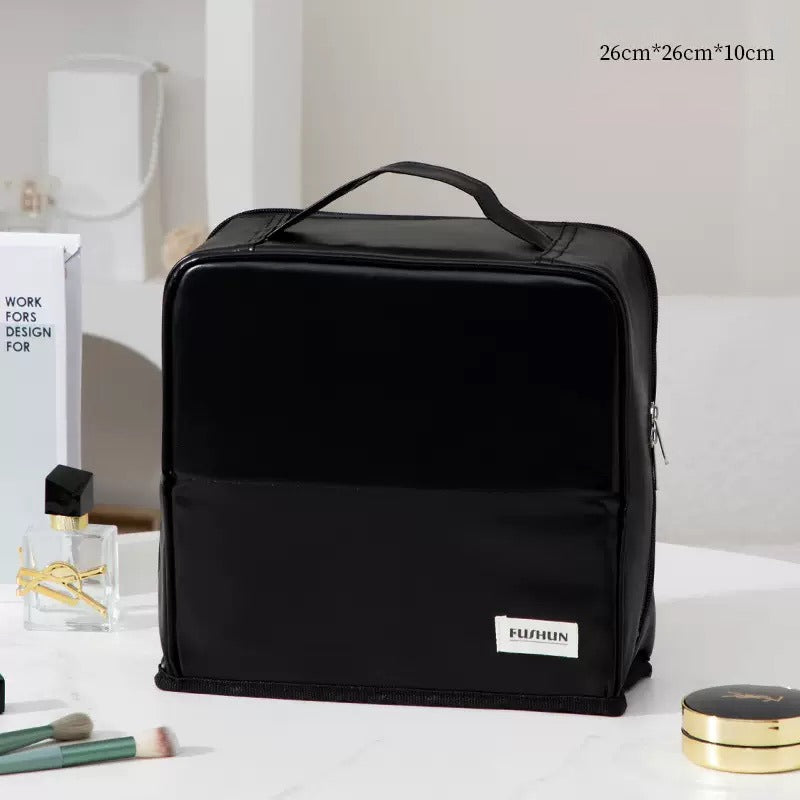 Travel Makeup Bag Cosmetic Organizer Case with a top handle sits on a white marble countertop. The bag features a white brand label reading 'FUSHUN' and is styled with beauty props like makeup brushes, a perfume bottle, and a compact mirror.