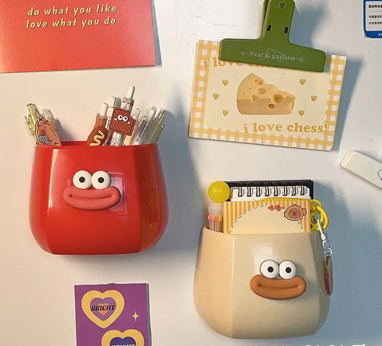 Two cute cartoon-style wall-mounted organizers with smiling faces, used to store pens, notes, and small items, adding a fun and colorful touch to the wall while keeping essentials organized.