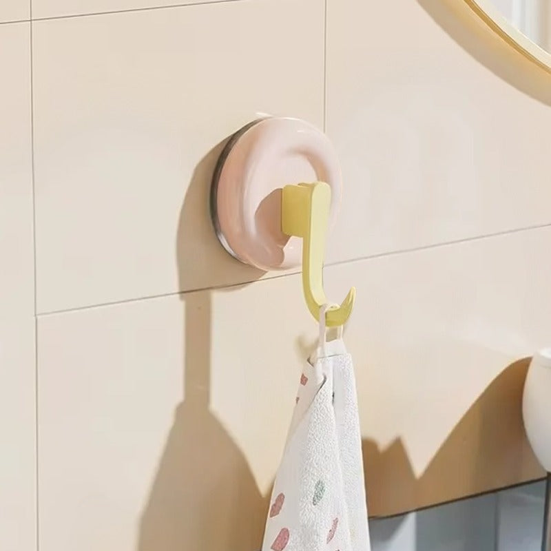 Wall-mounted hook with a pink base and yellow hook holding a towel against a beige tiled wall.