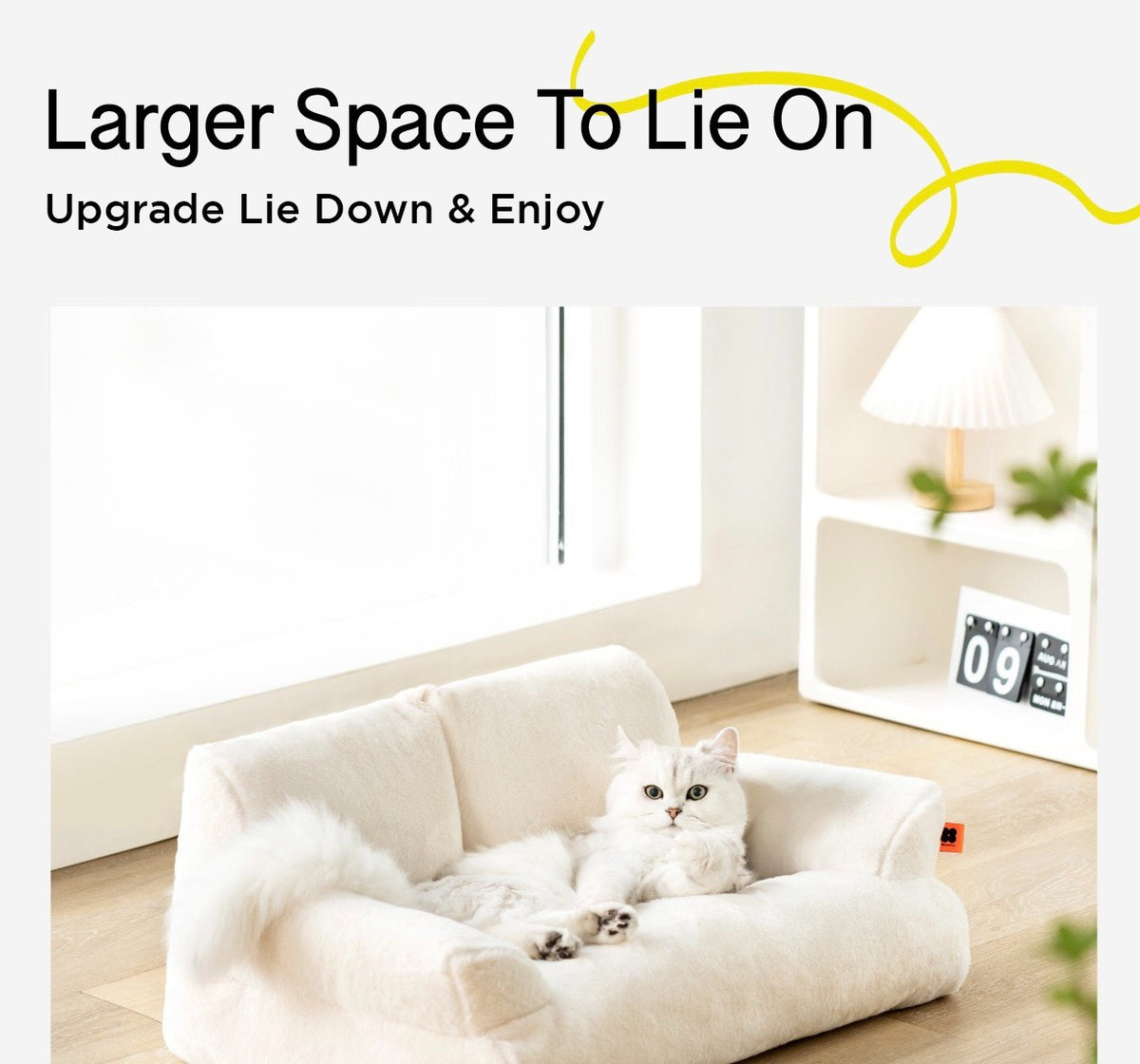 A cat lying on a white color Cat Sofa Couch Cushion next to a shelf with calendar and lamp in a room