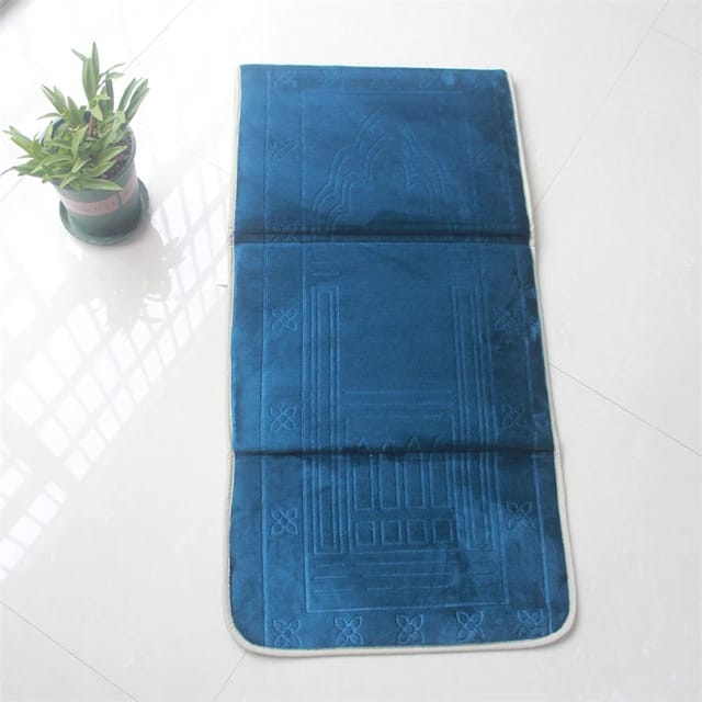 Fully opened Blue color Islamic Foldable Prayer Mat kept on a white surface next to a plant 