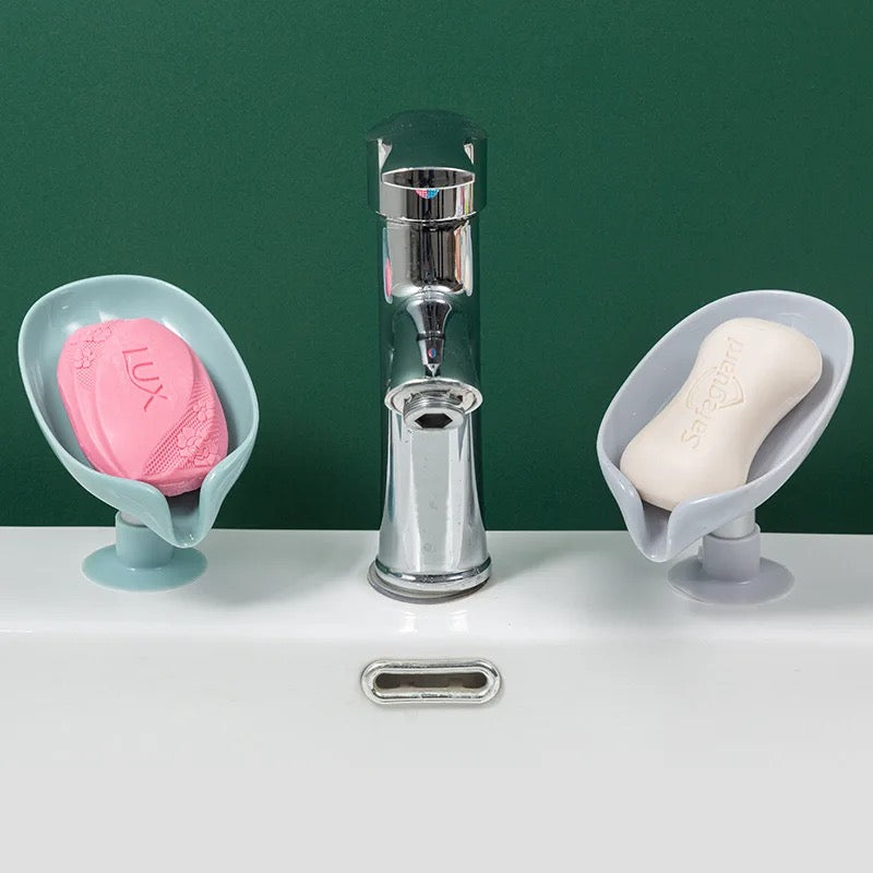 Two Leaf Shaped Soap Holders with soap kept on top of it been placed in left and right side of a wash basin faucet 