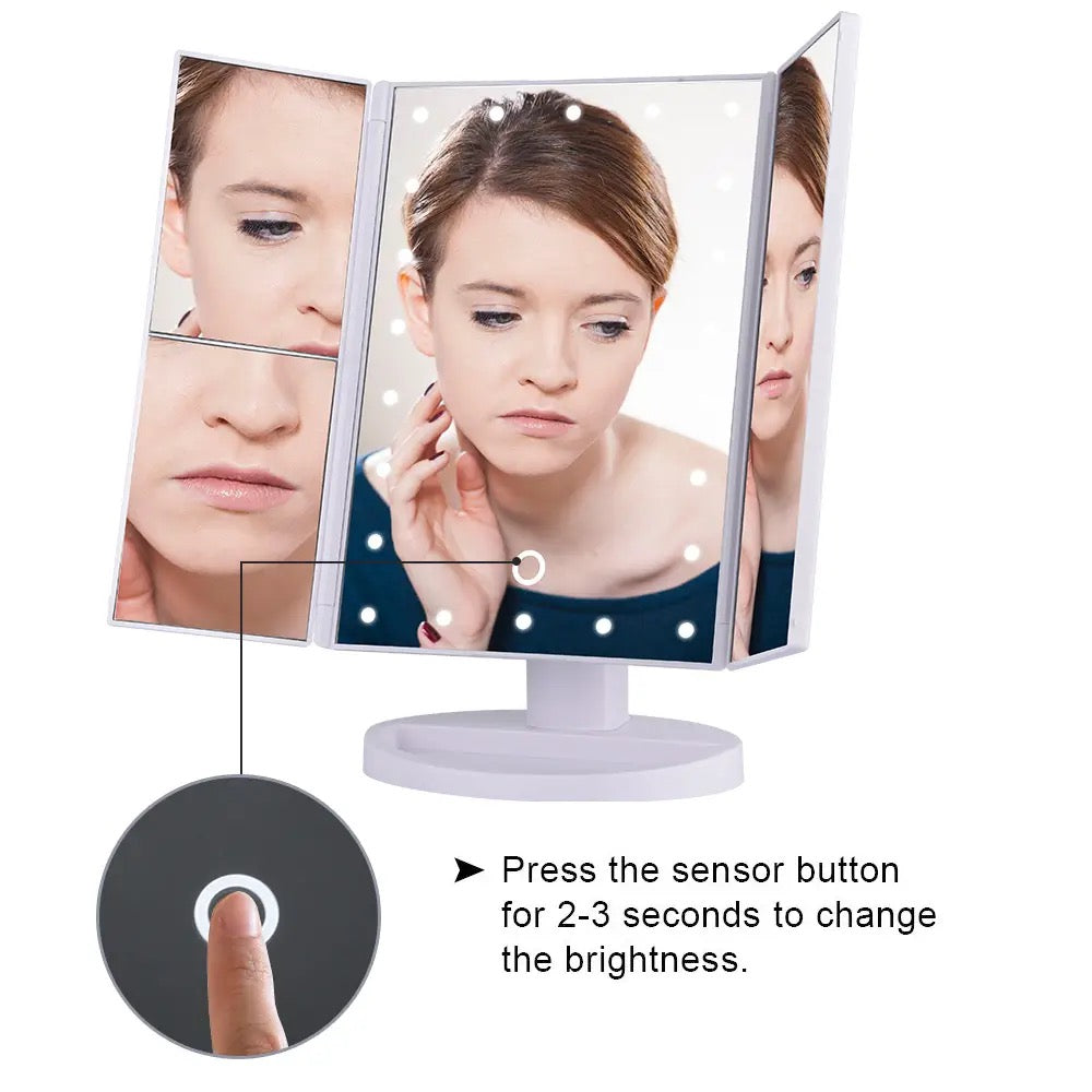 A woman examining her reflection in a tri-fold makeup mirror with LED lights