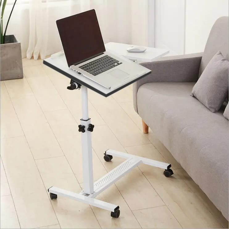 White Adjustable Overbed Laptop Stand Table with a laptop on top, positioned on the floor beside a sofa.