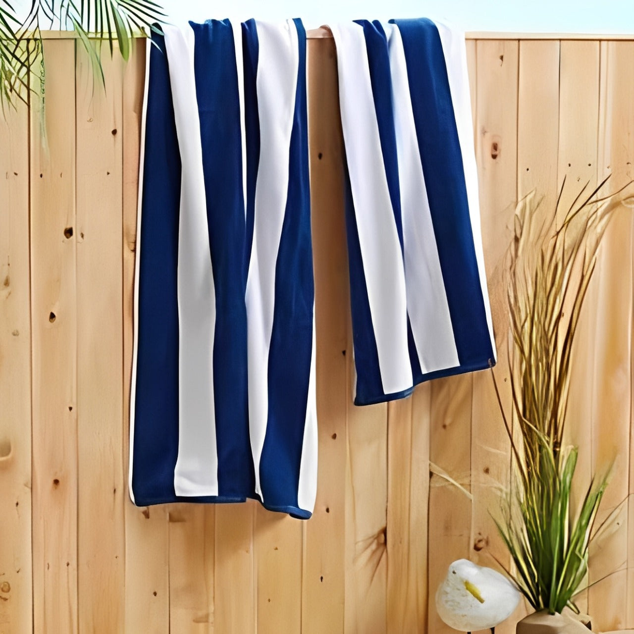 Blue and white striped towel hanging on a wooden fence with plants in the background