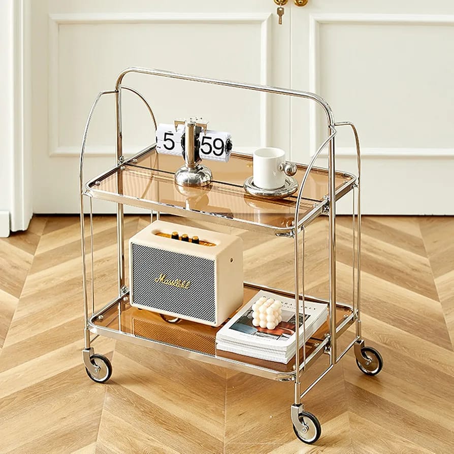  folding 2-tier serving trolley with a chrome finish, glass shelves, and rolling wheels arranged with a decor items.